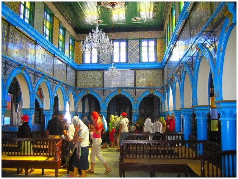 Interno della sinagoga El Ghriba con archi blu zellige e visitatori a Djerba